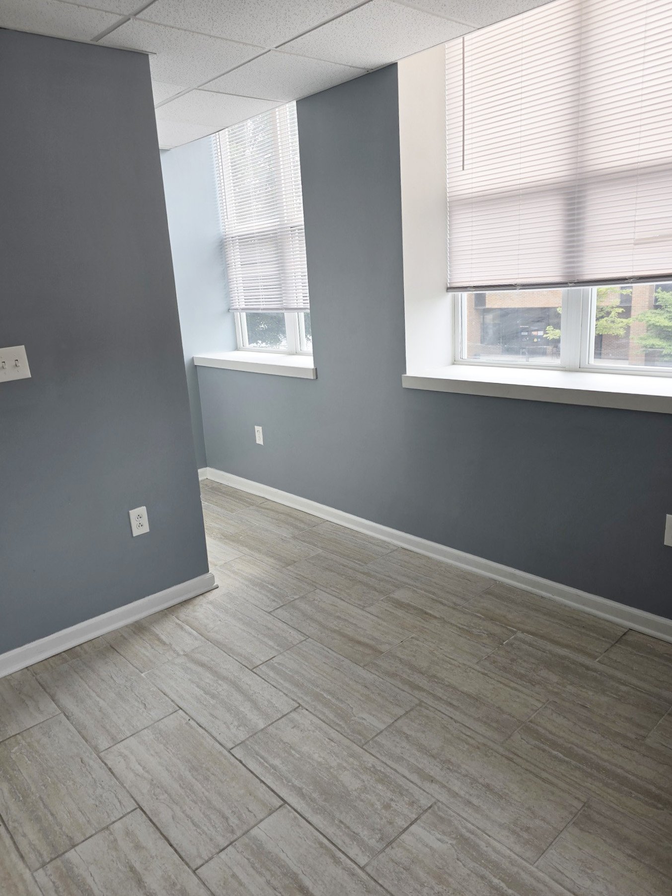 A room with a grey floor and a window with blinds.